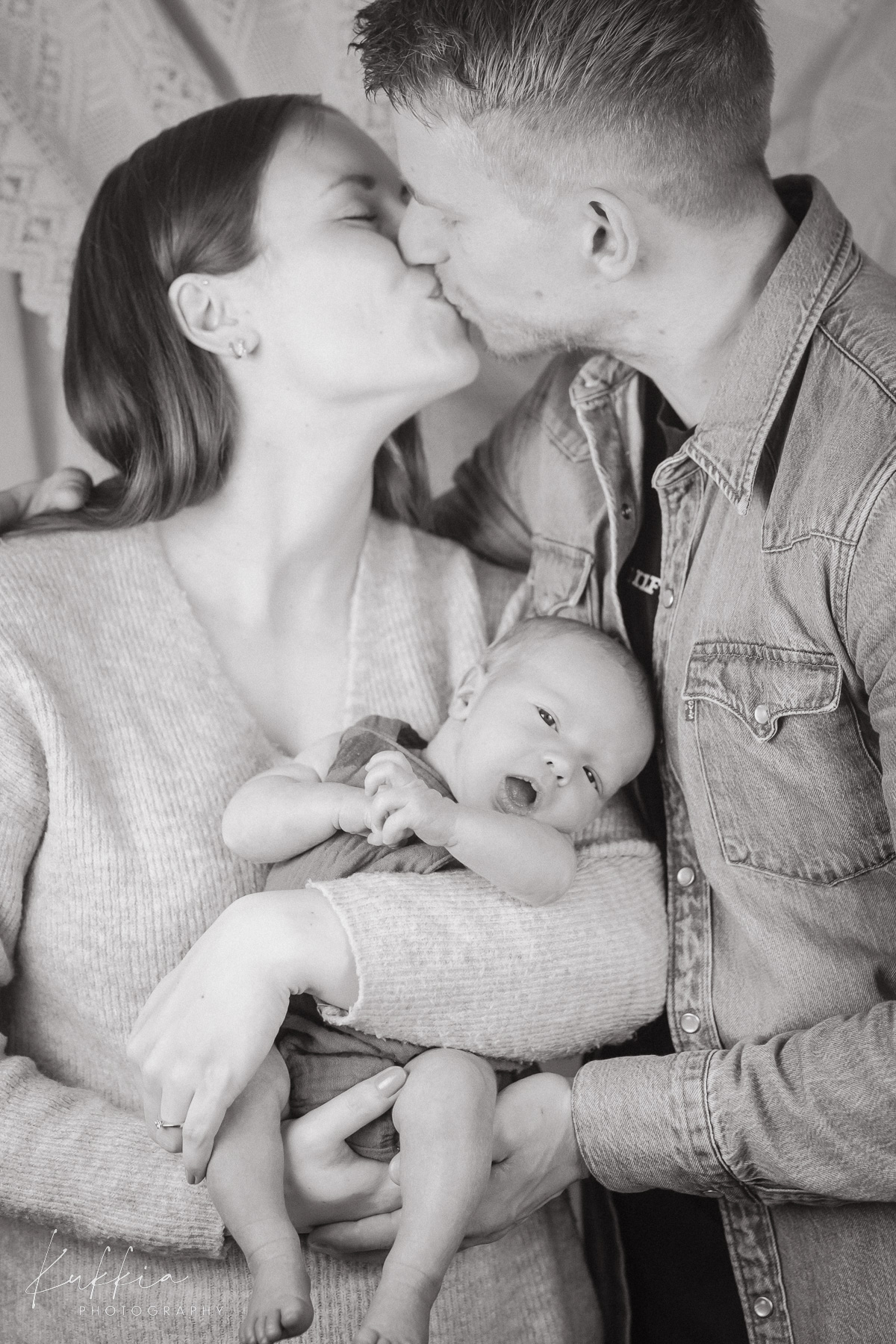 newborn-perhekuvaus-mustavalkoinen-aiti-isa-vauva.jpg Vanhemmat suutelevat toisiaan sylissään vastasyntynyt vauva mustavalkoisessa perhekuvassa